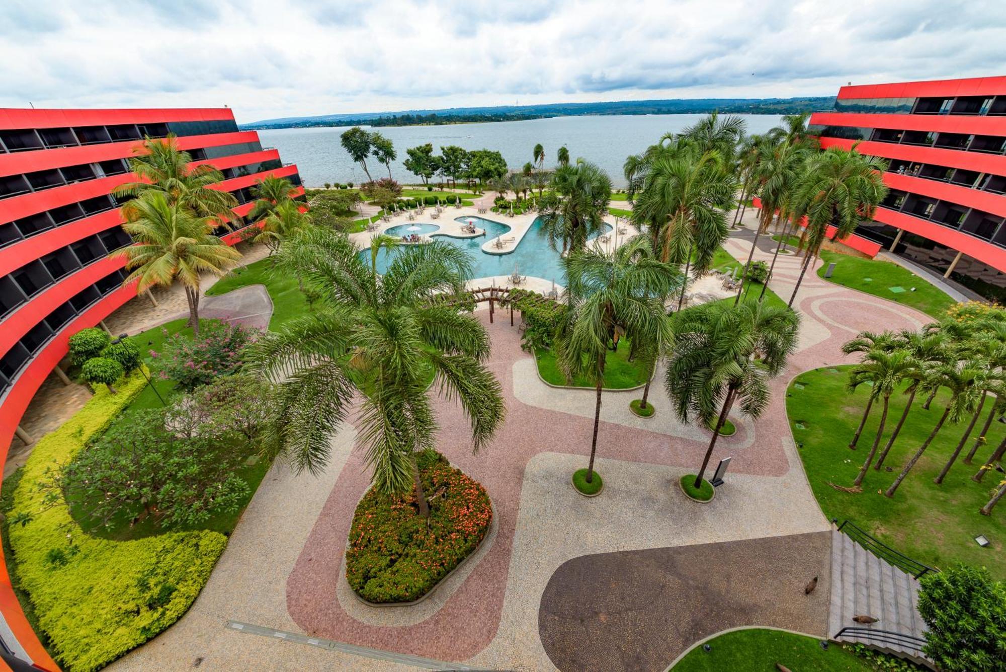 Royal Tulip Brasília Alvorada Hotel Exterior foto The photo shows a scenic view of a courtyard area in a residential complex. There are multiple red buildings surrounding a pool area, which is surrounded by palm trees and landscaped gardens. The pool features a curvy design, and there are pathways m